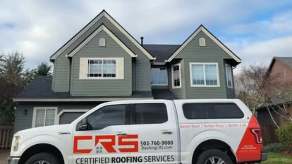 A white truck for CRS Certified Roofing Services, a roofing company in Portland, is parked in front of a gray house with a new dark shingle roof under a partly cloudy sky.